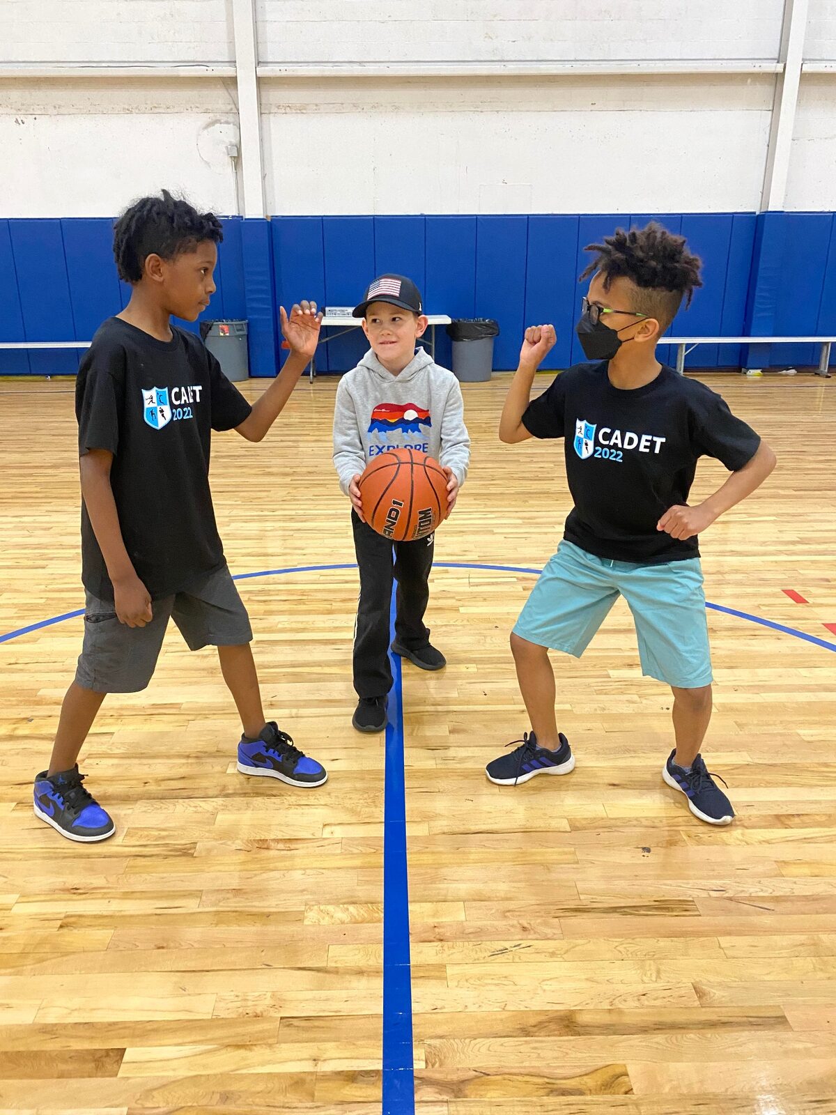 A Recreation Academy coach starting a basketball tip-off with two kids